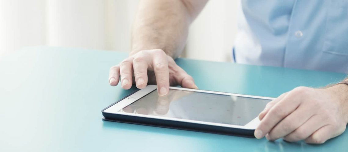Close-up panorama of a male doctor's hands on a table, checking medical history information of a patient on a tablet